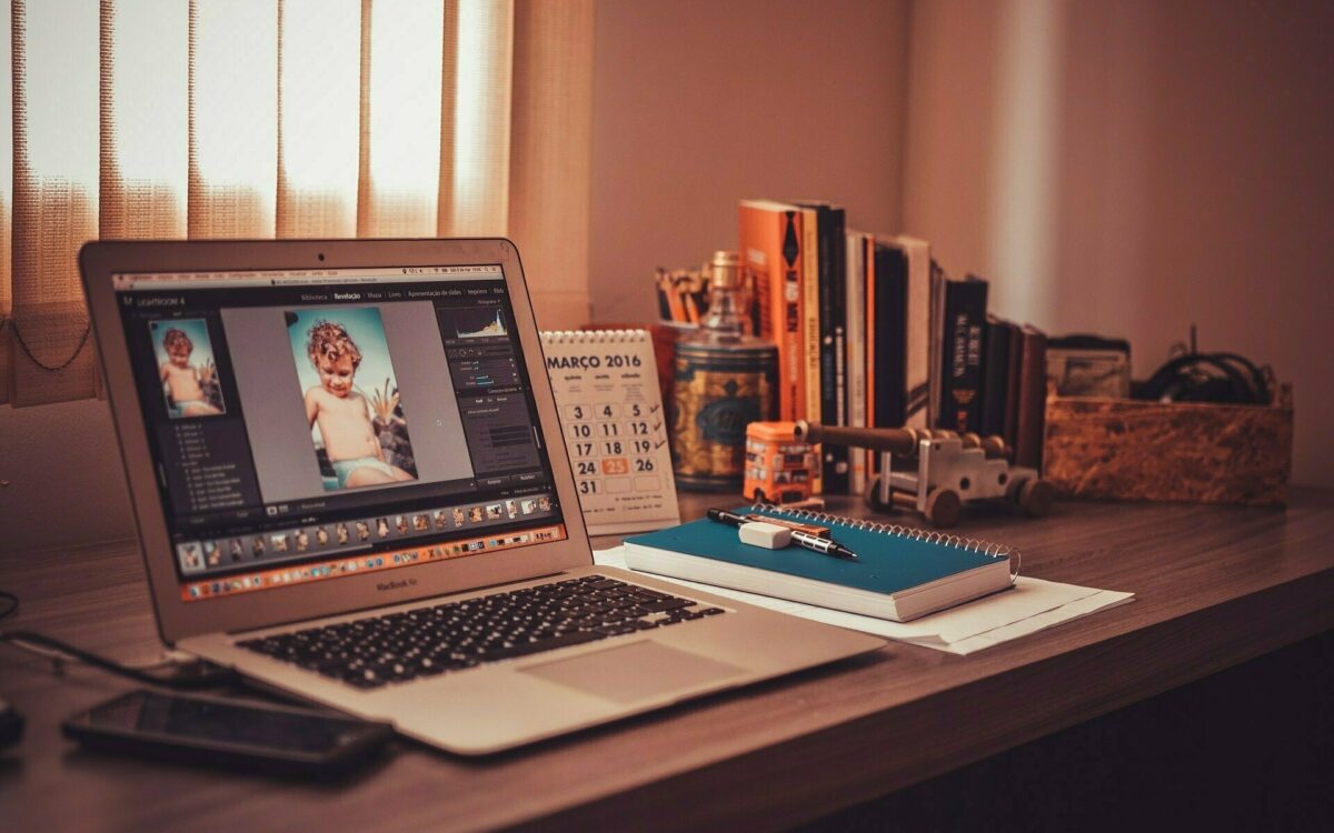 Homeoffice Arbeitsplatz mit aufgeklapptem Laptop, Notizbuch, Tischkalender und Stiften, der Schreibtisch steht vor Fenster mit Jalousien Homeoffice Arbeitsplatz mit aufgeklapptem Laptop, Notizbuch, Tischkalender und Stiften, der Schreibtisch steht vor Fenster mit Jalousien